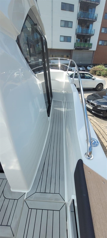 Wide view of a sleek boat deck with striped flooring, railings, and a building backdrop featuring parked cars.